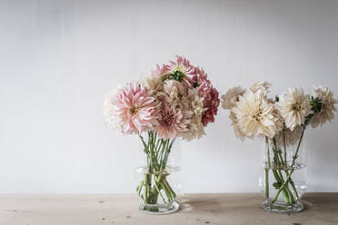 Holztisch mit Küchenutensilien und Blumensträußen in Vasen mit Wasser an einer weißen Wand - ADSF01814