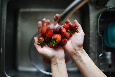 Crop weibliche Hände halten Drahtsieb mit hellen frischen Erdbeeren unter Waschbecken Wasserhahn auf hölzernen? counter von oben - ADSF01883