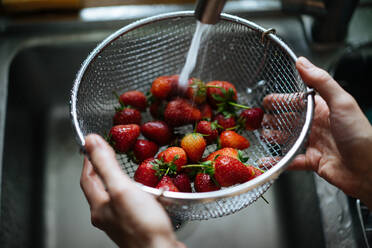 Crop weibliche Hände halten Drahtsieb mit hellen frischen Erdbeeren unter Waschbecken Wasserhahn auf hölzernen? counter von oben - ADSF01884