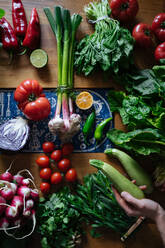 Crop view of female hands taking potherbs from elegant table with fresh healthy vegetable and fruit cooking ingredients from above - ADSF01894