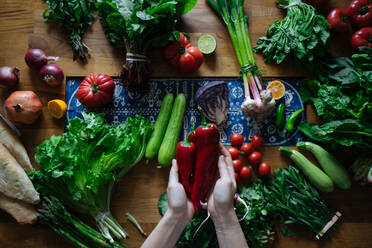 Crop view of female hands taking potherbs from elegant table with fresh healthy vegetable and fruit cooking ingredients from above - ADSF01895