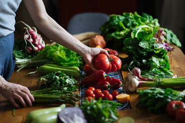 Crop view of female hands taking potherbs from elegant table with fresh healthy vegetable and fruit cooking ingredients from above - ADSF01897