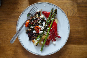 Tasty bright roasted potato with vegetables lying with green beans and fork on white plate with ornament on wooden table from above - ADSF01921