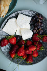 Schönes Set aus frischem Weichkäse mit Erdbeeren und Kirschen auf strukturiertem dunklem Teller auf blauem Tisch von oben liegend - ADSF01940