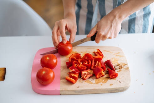 Crop-Ansicht einer Frau in Sommerkleidung, die leckere frische Tomaten auf einem Holzbrett schneidet, während andere Zutaten auf dem Tisch liegen - ADSF01943