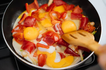 Crop back view of?woman hands cracking egg into frying pan with sliced red vegetables - ADSF01945