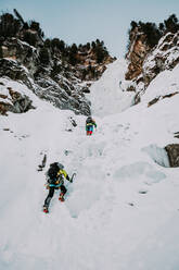Von unten Rückenansicht Menschen mit Ausrüstungen Montage auf Schnee Klippe mit Wald an der Spitze in Deutschland - ADSF01983