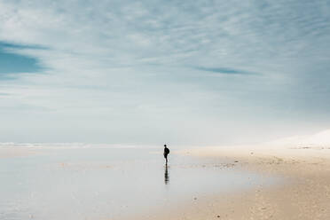 Side view person with backpack standing on shore near water and beautiful heaven with clouds in France - ADSF01993