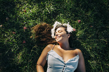 Young woman with eyes closed relaxing on grassy land in park during sunny day - DCRF00464