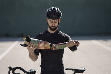 Handsome bearded man in helmet holding arm prosthesis while standing near bike - ADSF02063
