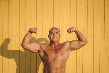 Muscular older man poses yellow background. - ADSF02085