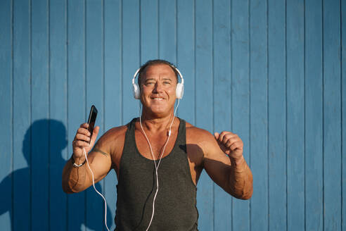 Starker älterer Mann posiert mit Kopfhörern auf blauem Hintergrund. - ADSF02090