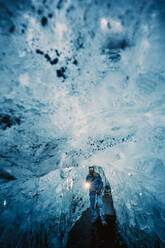 Traveler with burning torch standing in hall of crystal blue ice cave, Iceland - ADSF02100