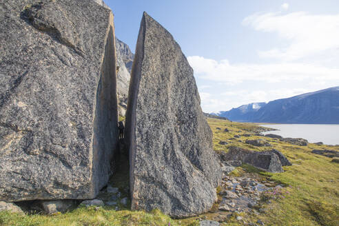 Backpacker squeezes through split in giant cracked boulder. - CAVF87338