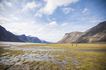 Two backpackers cross wet tundra in Akshayak Pass. - CAVF87360