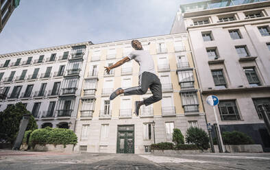 Afrikanischer Mann im Hemd springt vor Gebäude. - ADSF02127