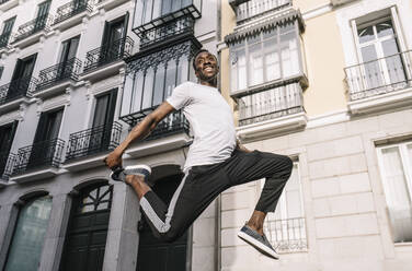 Afrikanischer Mann im Hemd springt vor Gebäude. - ADSF02129