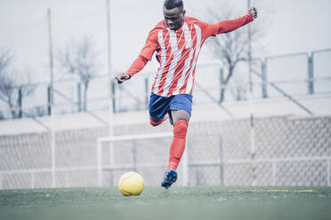 Afrikanischer Fußballspieler mit roter und weißer Ausrüstung beim Fußballspielen. - ADSF02193