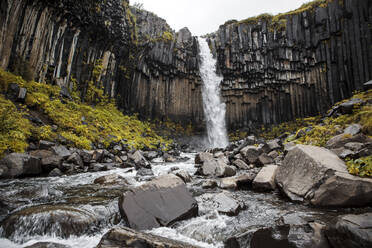 Blick von unten auf eine mächtige Kaskade mit Steinhang und Bach in Island - ADSF02217