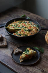 Plate and metal saucepan with delicious pumpkin and spinach frittata standing on timber tabletop - ADSF02285