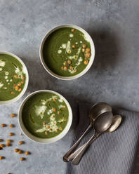 From above bowls with tasty green vegetable cream soup with nuts near spoons on napkin on grey background - ADSF02298