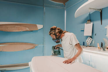 Mann mit Werkzeug beim Sägen eines Surfbretts in einer Werkstatt - ADSF02323