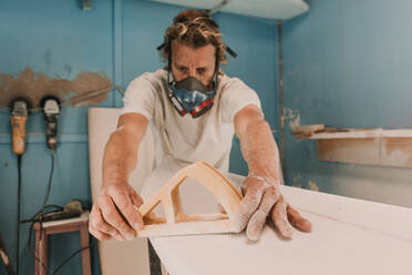 Mann mit Atemschutzmaske poliert Surfbrett in Werkstatt - ADSF02324