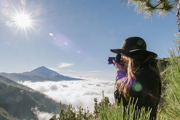 Seitenansicht einer Fotografin, die auf dem Gipfel eines Hügels steht und die Wolkenlandschaft an einem sonnigen Tag fotografiert - ADSF02338