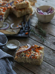 Kleine Stücke leckerer Focaccia mit Kürbis und Zwiebeln liegen auf einer verwitterten Holztischplatte neben Schere und Salz mit Rosmarin - ADSF02371