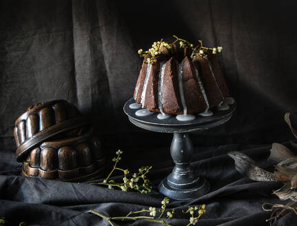 Ständer mit serviertem veganem Schokoladenkuchen auf schwarzem Stoff mit grünen Pflanzenzweigen - ADSF02459