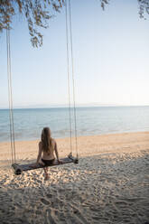 Attractive woman sitting on swings on sandy shore in Thailand. - ADSF02477