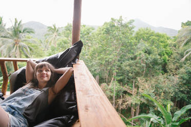 Fröhliche junge Frau, die auf einer Terrasse in einem tropischen Wald liegt und in Thailand wegschaut. - ADSF02484