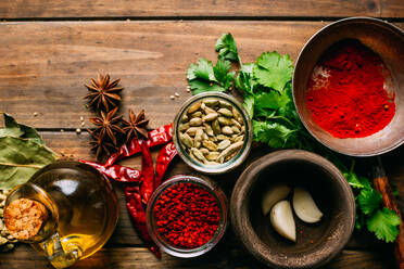 Assorted spices and herbs and bottle of oil placed on wooden tabletop - ADSF02489