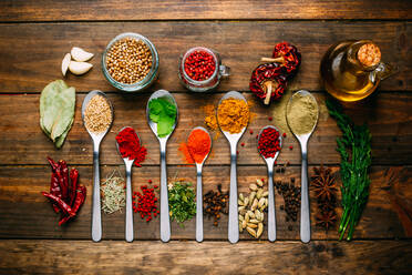 Bunch of assorted spices placed in order on lumber tabletop near bottle of oil - ADSF02496