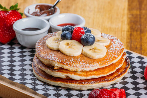 Leckere gebratene fluffige Pfannkuchen mit Puderzucker und frischen Beeren zum Frühstück - ADSF02503