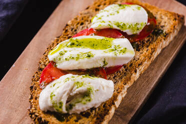 Nahaufnahme von goldenem Toastbrot mit Tomaten und Weißkäse, belegt mit grüner Soße. - ADSF02516