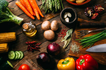 Assorted fresh vegetables and bottle of oil lying on timber tabletop near various cooking tools - ADSF02519