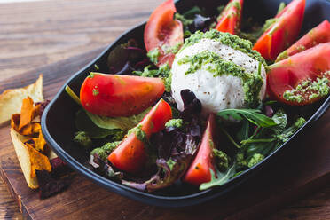 Nahaufnahme von serviertem Salat mit Tomaten in grüner Soße auf einem Haufen Grün mit einer Kugel Käse. - ADSF02528