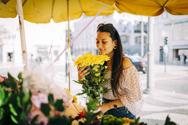 Junge Frau riecht an einem Blumenstrauß in einem Blumenladen - DCRF00480