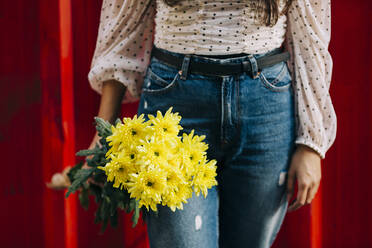 Close-up of woman holding flowers against red wall - DCRF00483