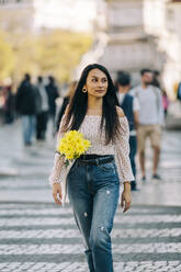 Young woman with bouquet walking on street in city - DCRF00485