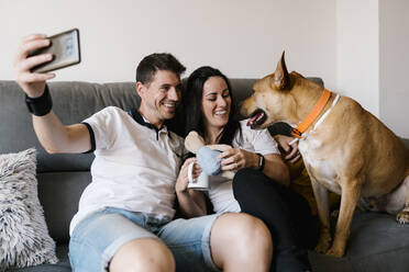 Lächelndes Paar macht Selfie mit Hund zu Hause - EGAF00434