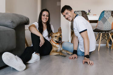 Man and woman sitting with dog on floor at home - EGAF00443
