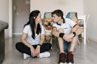 Couple kissing dog while sitting on floor at home - EGAF00445