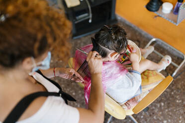 Hairdresser cutting wet hair of flittle girl searching clips in basket - EGAF00471