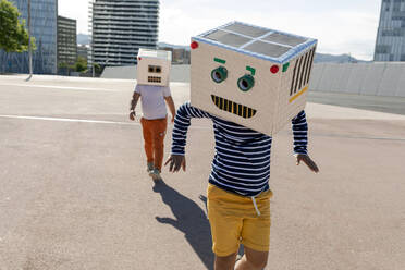 Carefree boy wearing robot mask dancing while friend walking on street in city - VABF03134