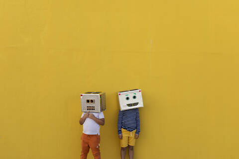 Boys wearing robot masks made of boxes while standing against yellow wall stock photo