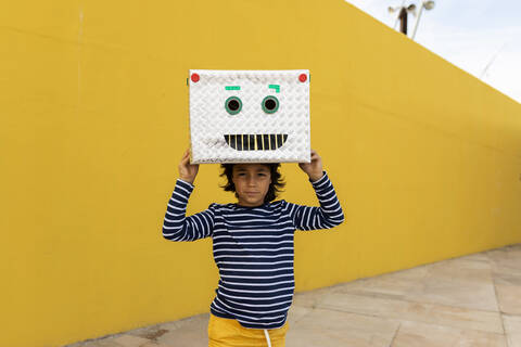 Boy wearing robot mask while standing against yellow wall stock photo