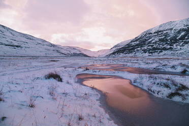 Blick auf ruhiges Gelände mit gefrorenen See unter Schnee zwischen Bergen auf dem Hintergrund des Sonnenuntergangs rosa Himmel - ADSF02661