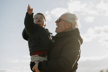 Aged man carrying grandson in arms - ADSF02668